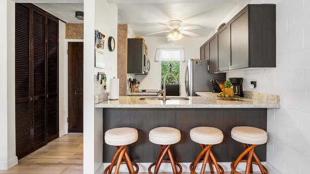 A kitchen with dark cabinets, a granite countertop, and four stools.
