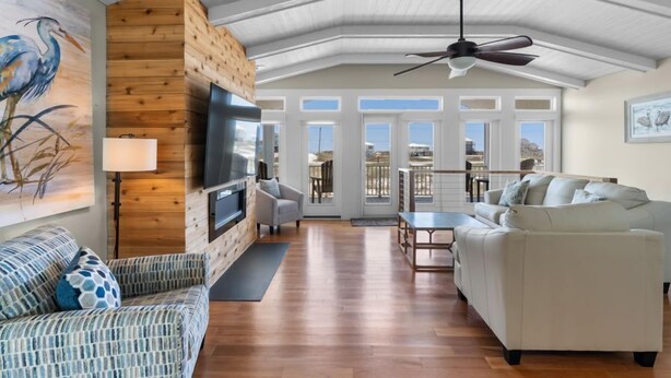 A spacious living room with a wooden accent wall, a flat-screen TV, a ceiling fan, and a large window offering a view of the outdoors. - Lagoon Front | Boat Dock & Fishing Pier | Sleeps 12 (Gulf Shores)