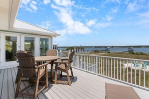 A deck with a table and chairs, overlooking a body of water with a pier and dock.