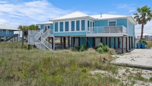 A beachfront house with a covered porch, a staircase leading to a balcony, and a sandy beach in the background. - Lagoon Front | Boat Dock & Fishing Pier | Sleeps 12 (Gulf Shores)