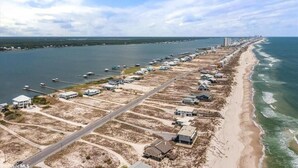 An aerial view of a coastal area with a long stretch of beach, a marina with boats, and a row of buildings along the shore. - Lagoon Front | Boat Dock & Fishing Pier | Sleeps 12 (Gulf Shores)