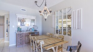 Uma área de refeições com uma mesa e cadeiras de madeira, um lustre, um espelho e uma janela com persianas.