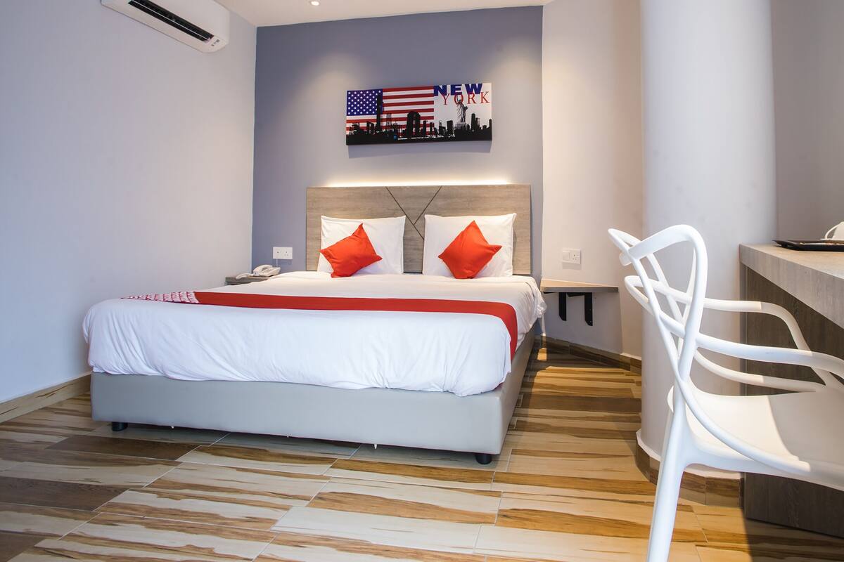 Une chambre d’hôtel avec un lit, un bureau et une chaise. Un tableau représentant la vue panoramique de New York est accroché au mur.