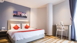 Ein Hotelzimmer mit einem Bett, einem Schreibtisch und einem Sessel. An der Wand hängt ein Bild der Skyline von New York.