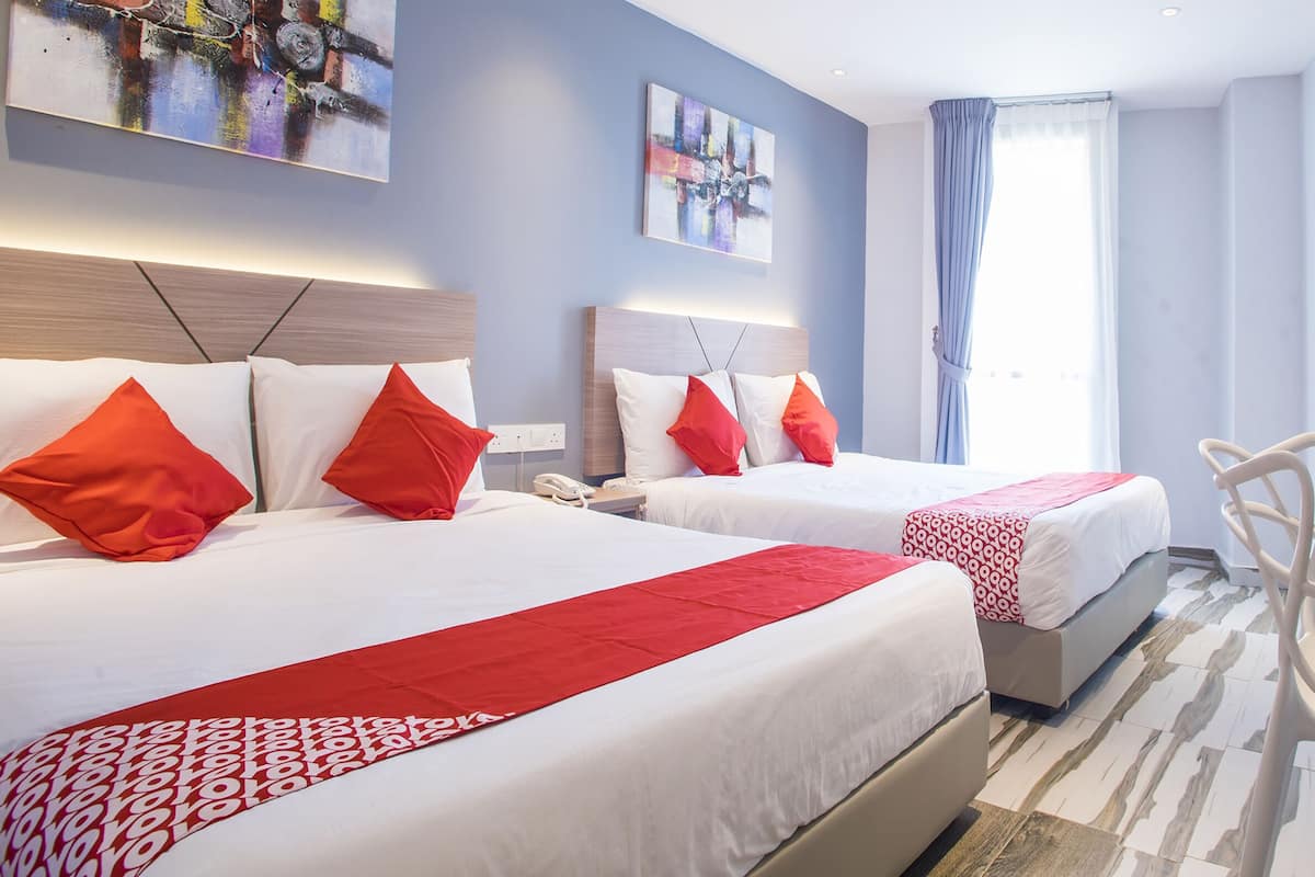 Une chambre d’hôtel avec deux lits, chacun agrémenté de draps rouges et blancs, d’une tête de lit moderne et d’un grand tableau abstrait accroché au mur.