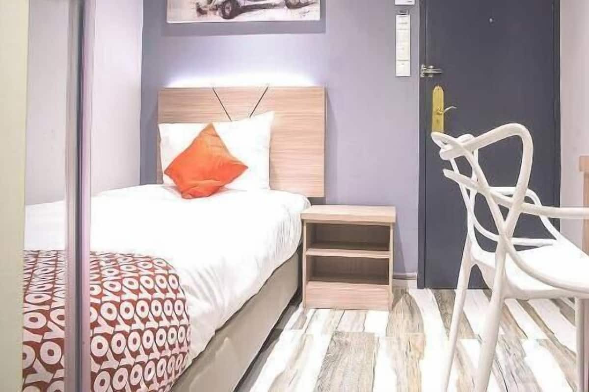 Um quarto com uma cama, uma mesa de cabeceira, uma cadeira e uma porta.