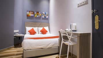 A hotel room with a bed, a bedside table with a phone, a chair, a desk with a coffee maker, and artwork on the wall.