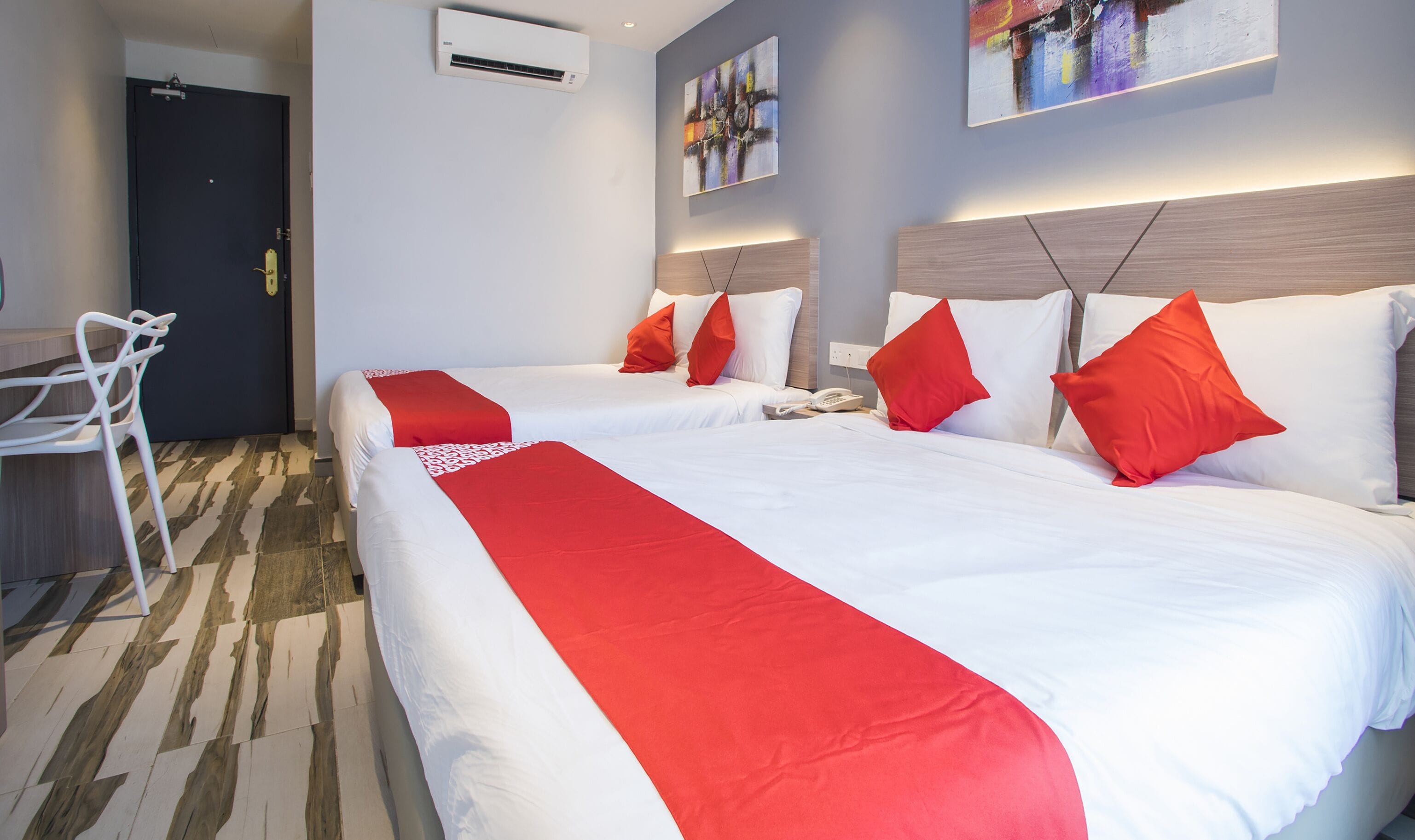 Habitación de hotel con dos camas, ropa de cama roja y blanca, un escritorio y una silla.