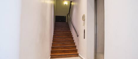 A narrow hallway with a wooden staircase leading to a door.