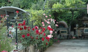 Un jardin où l’on peut admirer une grande variété de roses, une clôture en métal et, au fond, une construction en briques.