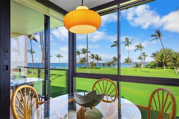 Una habitación con un ventanal grande que da a un campo de golf y palmeras, una mesa redonda con sillas y una lámpara colgante.