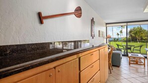 Une cuisine dotée de meubles en bois, d’un plan de travail en granit et offrant une vue sur un patio aménagé avec du mobilier d’extérieur.