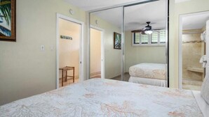 A bedroom with a bed, a small stool, a mirror, and a shower area. - Kihei Surfside #213: Oceanfront Charm and Comfort with Breathtaking Views (Kihei, Maui)
