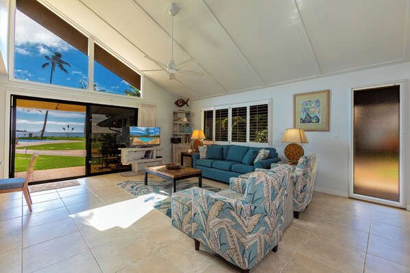 A spacious living room with a large window, a ceiling fan, a blue sofa, and a television.