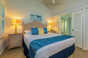 Un dormitorio con una cama, dos mesitas de noche con lámparas, una mesita auxiliar, una puerta y una obra de arte colgada en la pared.
