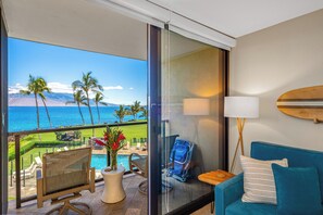 A balcony with a view of the ocean, a pool, and lounge chairs.
