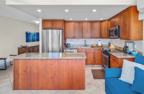 A modern kitchen with wooden cabinets, stainless steel appliances, and a granite countertop. - Kihei Surfside #304 - Spectacular Oceanfront, A/C, 2 Sofa Beds; 1/1.5 baths (Kihei, Maui)