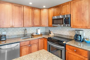 Una cocina con gabinetes de madera, lavavajillas de acero inoxidable, horno empotrado, microondas y encimera de granito.