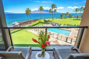 A balcony with a view of a pool, a grassy area, and the ocean.