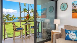 Ein Balkon mit Blick auf einen Golfplatz und Palmen, ein Sofa mit Kissen in Form einer Schildkröte und eine Wanduhr.