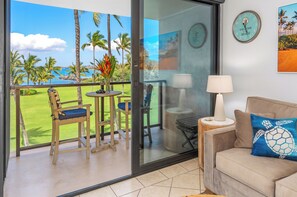 Un balcon donnant sur un terrain de golf et des palmiers, un canapé avec un coussin en forme de tortue et une horloge murale.
