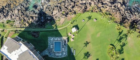 Eine Vogelperspektive zeigt ein Resort mit Schwimmbad, Liegebereich und Palmen.