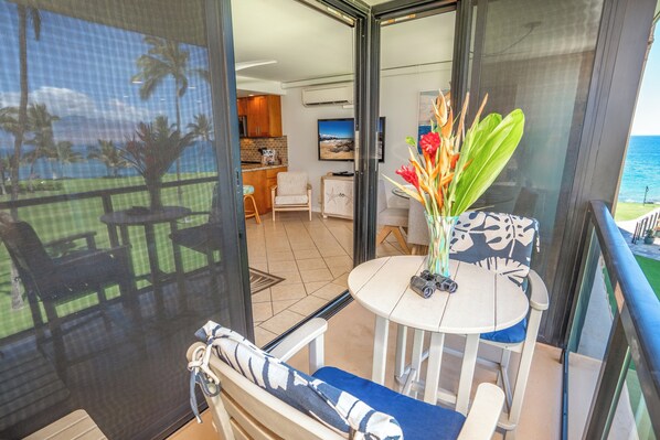 A balcony with a table and chairs, a view of the ocean, and a glimpse of the interior including a kitchen and a dining area. - Exquisite Oceanview - Kihei Surfside #310 - Your Gateway to Maui Bliss! (Kihei, Maui)