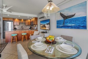 A modern kitchen with wooden cabinets, a stainless steel refrigerator, and a dining area with a glass table set for four.