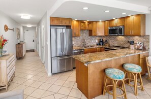 A modern kitchen with wooden cabinets, stainless steel appliances, and a granite countertop. - Exquisite Oceanview - Kihei Surfside #310 - Your Gateway to Maui Bliss! (Kihei, Maui)