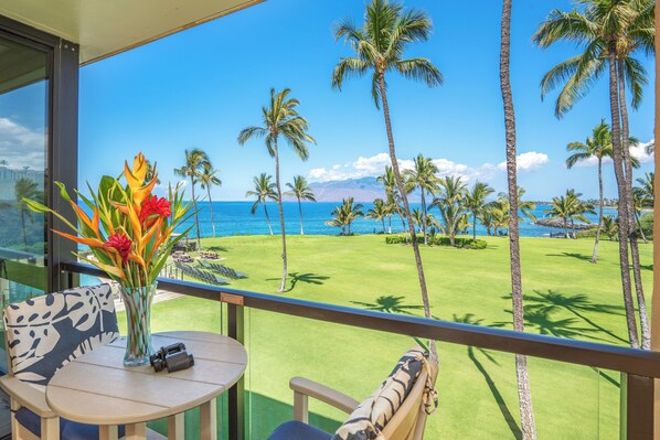 A balcony with a view of a golf course, palm trees, and the ocean.