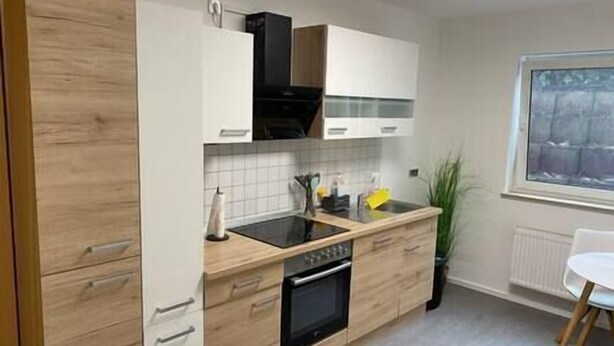 A modern kitchen with wooden cabinets, a black stove, and a window with a view. - Apartment in the countryside near Koblenz, Apartment im Grünen bei Koblenz (Vallendar)