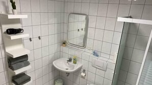 A bathroom with a white sink, toilet, and shower. There are shelves with towels and toiletries. - Apartment in the countryside near Koblenz, Apartment im Grünen bei Koblenz (Vallendar)