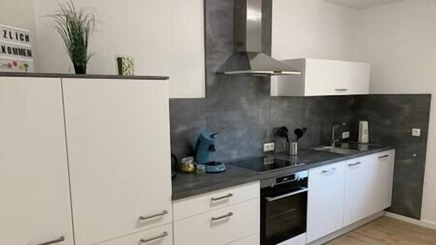 Une cuisine moderne avec des meubles blancs, une cuisinière noire et un pare-feu gris.