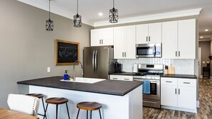 A modern kitchen with white cabinets, a central island with stools, stainless steel appliances, and pendant lighting. - Historic charm Modern Luxury (Batesville)