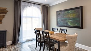 A dining room with a wooden table, six chairs, a large window with sheer curtains, a painting on the wall, and a dark wooden cabinet. - Historic charm Modern Luxury (Batesville)