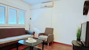 A modern living room with a sofa, armchair, coffee table, and a TV. - Lovely ground floor apartment with a sunny terrace (Mostar)