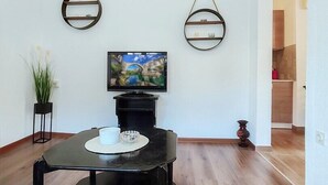 A modern living room with a black coffee table, a flat-screen TV mounted on the wall, and two wall-mounted shelves. - Lovely ground floor apartment with a sunny terrace (Mostar)