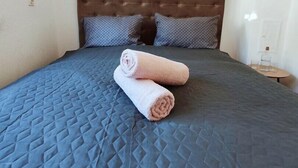 A neatly made bed with a quilted blue bedspread, two rolled towels, and a wooden headboard. - Lovely ground floor apartment with a sunny terrace (Mostar)