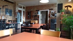 A dining area with brick walls, wooden tables, and chairs. There are hanging lights and a potted plant. - L'Ermite (Saint-Algis)