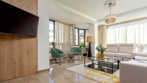 Een moderne woonkamer met een flatscreen televisie, twee groene fauteuils, een witte bank, een salontafel en een lamp.