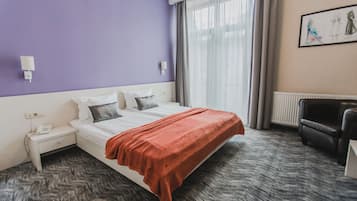 Habitación de hotel con cama, mesita de noche con teléfono, una silla y ventana con cortinas.