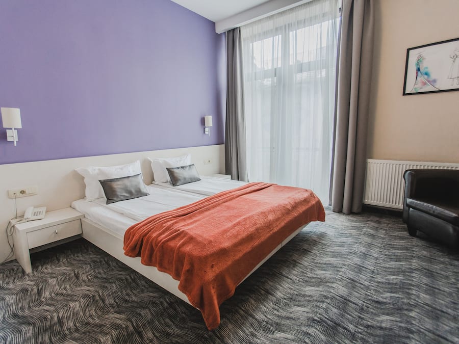 Habitación de hotel con cama, mesita de noche con teléfono, una silla y ventana con cortinas.