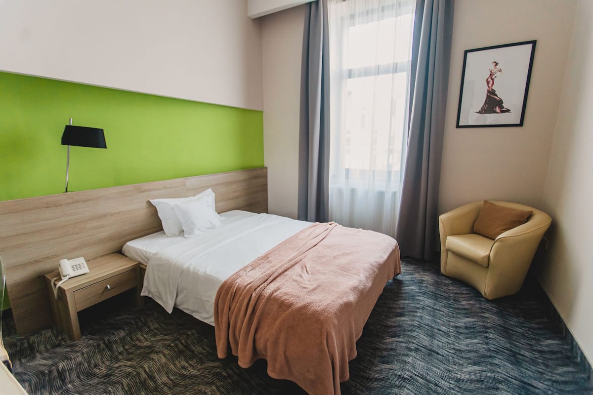A hotel room with a bed, a nightstand, a chair, a lamp, and a window with curtains.