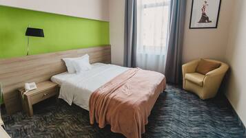 A hotel room with a bed, a nightstand, a chair, a lamp, and a window with curtains.