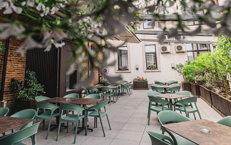 An outdoor patio with green chairs and tables, brick walls, and potted plants.