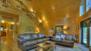 A spacious log cabin interior with a large leather sofa, a coffee table, and a staircase leading to an upper level. - Escape to Tranquility: Sleepy Hollow Cabin Retreat (Ellijay)