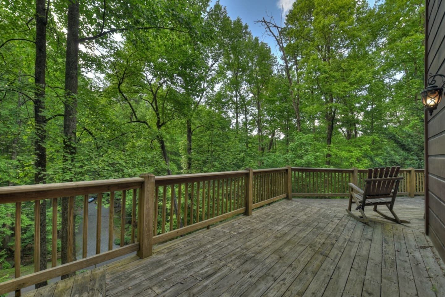 A wooden deck with a wooden railing, a rocking chair, and a lantern on the right side.