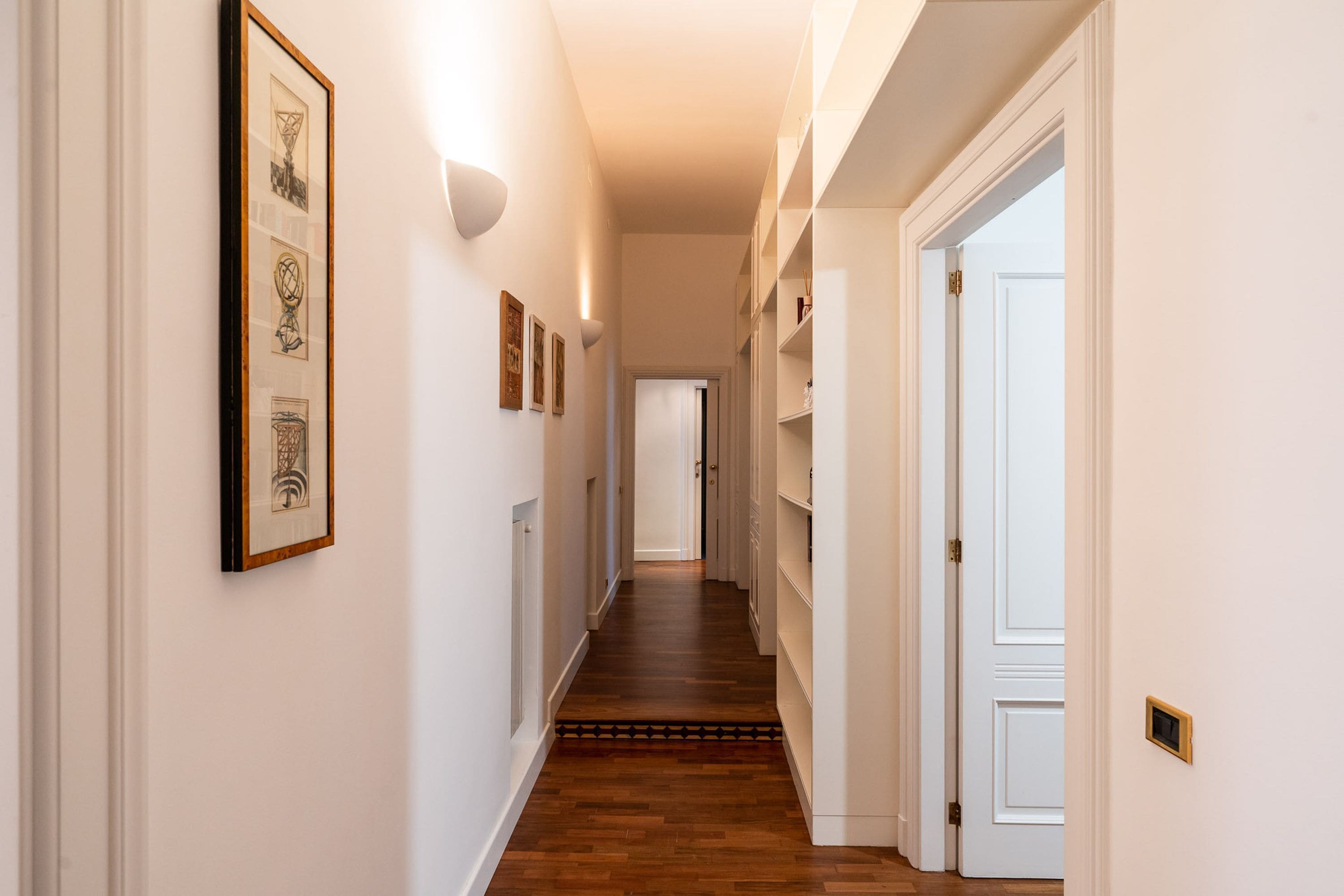 A hallway with wooden flooring, white walls, and framed artwork.