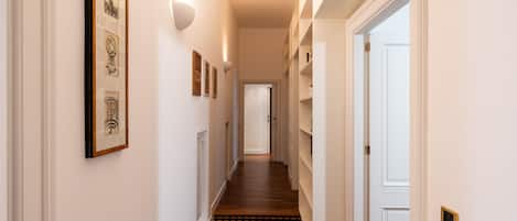 A hallway with wooden flooring, white walls, and framed artwork.