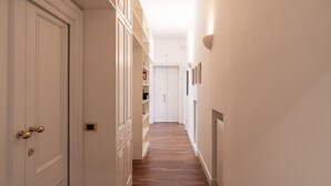 En smal hall med vita väggar och trägolv, som leder fram till en dörr i slutet.